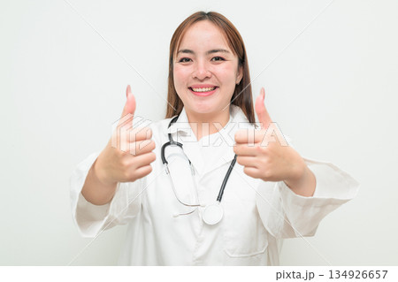 Portrait of young Asian female doctor against white background giving thumbs up gesture Portrait of young Asian female doctor against white background giving thumbs up gesture 134926657