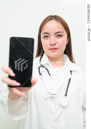Young Asian female doctor against white background showing phone device screen with copy space 134926699