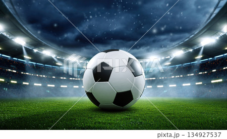 Soccer ball sits in the center of the field at a stadium during a night match under the lights and overcast sky Soccer ball sits in the center of the field at a stadium during a night match under the lights and overcast sky 134927537