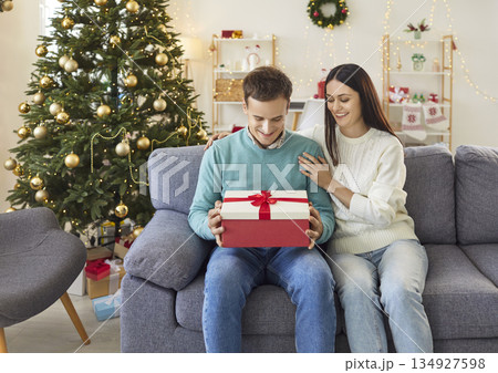 Young woman congratulating man boyfriend on Christmas holiday with present gift box at home. Young woman congratulating man boyfriend on Christmas holiday with present gift box at home. 134927598