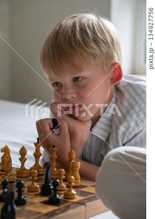Young boy rests his chin on his hands while studying chessboard at home, showing focus, curiosity, thoughtful mood in soft natural light Young boy rests his chin on his hands while studying chessboard at home, showing focus, curiosity, thoughtful mood in soft natural light 134927756