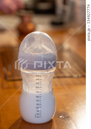 Baby bottle filled with milk stands on a wooden kitchen countertop, showing clear measurement marks, soft colors, and a calm everyday home mood Baby bottle filled with milk stands on a wooden kitchen countertop, showing clear measurement marks, soft colors, and a calm everyday home mood 134927774