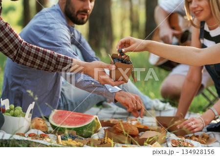Sharing the meal. Group of friends are having picnic on the field with food in eco boxes Sharing the meal. Group of friends are having picnic on the field with food in eco boxes 134928156