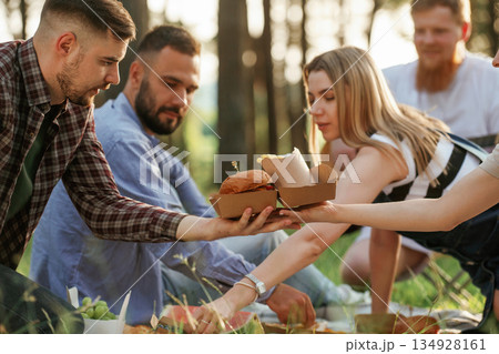 Yummy meal, sitting. Group of friends are having picnic on the field with food in eco boxes 134928161