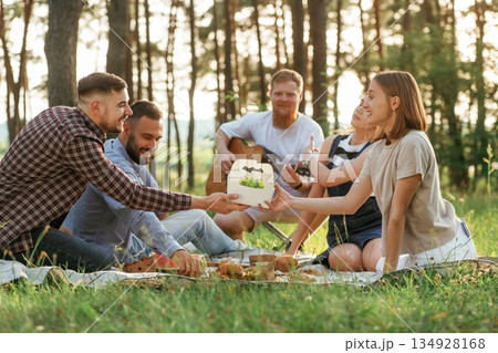 On the ground. Group of friends are having picnic on the field with food in eco boxes On the ground. Group of friends are having picnic on the field with food in eco boxes 134928168