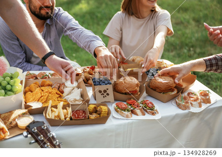Enjoying the meal. Group of friends are having picnic on the field with food in eco boxes Enjoying the meal. Group of friends are having picnic on the field with food in eco boxes 134928269