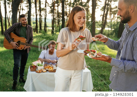 Tasty meal in hands. Group of friends are having picnic on the field with food in eco boxes Tasty meal in hands. Group of friends are having picnic on the field with food in eco boxes 134928301