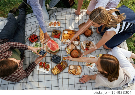 Fresh products, sitting. Group of friends are having picnic on the field with food in eco boxes Fresh products, sitting. Group of friends are having picnic on the field with food in eco boxes 134928304
