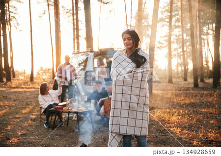 Woman in blanket, standing by bonfire with smoke. Group of friends are together in the forest 134928659