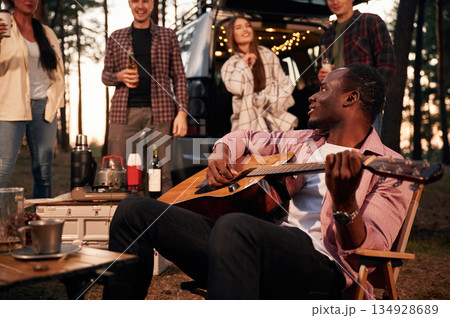 Acoustic guitar player. Group of friends are together in the forest Acoustic guitar player. Group of friends are together in the forest 134928689