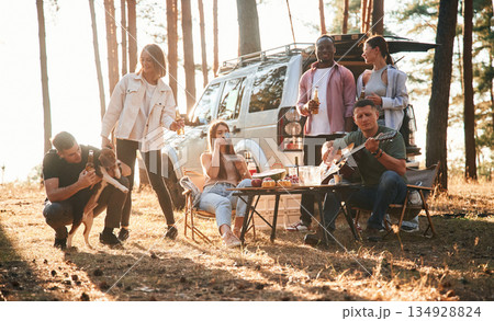 Drinking, eating, playing with dog. Group of friends are together in the forest 134928824