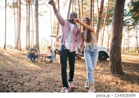 Couple are holding each other by the hands, walking. Group of friends are together in the forest 134928899