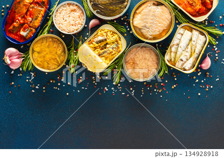 Different open tin cans with canned fish like salmon, mackerel, sprat, sardine, tuna, and herring, among spices and herbs on a blue background, viewed from the top Different open tin cans with canned fish like salmon, mackerel, sprat, sardine, tuna, and herring, among spices and herbs on a blue background, viewed from the top 134928918