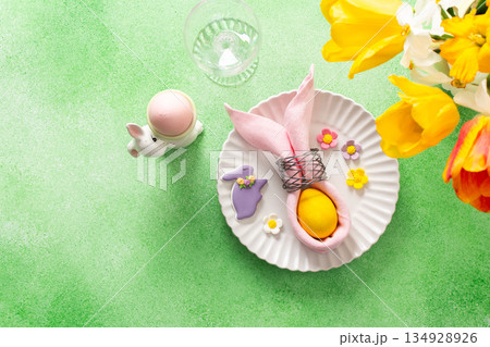 A beautifully arranged Easter table setting showcases a decorative egg nestled in a pink napkin, surrounded by a glass of water and fresh flowers, perfect for holiday gatherings A beautifully arranged Easter table setting showcases a decorative egg nestled in a pink napkin, surrounded by a glass of water and fresh flowers, perfect for holiday gatherings 134928926