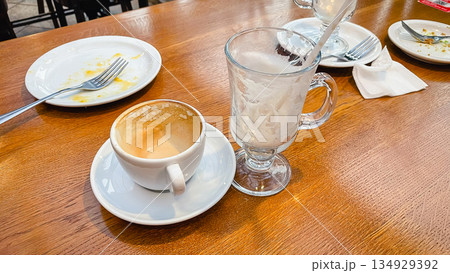 Empty coffee cup and glass mug with dirty plates on a wooden table after breakfast in a cafe 134929392