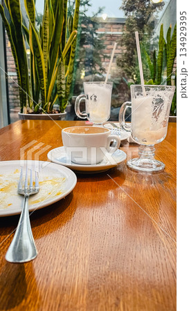 Empty coffee cups and a dirty plate with a fork on a wooden table after breakfast in a cozy cafe Empty coffee cups and a dirty plate with a fork on a wooden table after breakfast in a cozy cafe 134929395