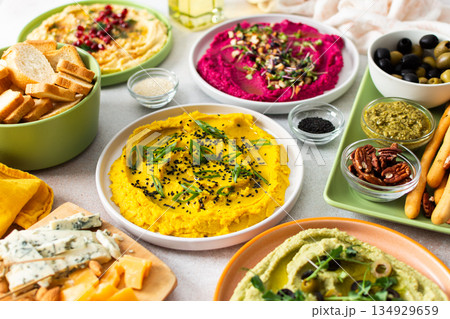 A variety of hummus flavors including turmeric, classic, and broccoli are served with fresh bread, nuts, and garnishes on a colorful charcuterie board, perfect for sharing 134929659