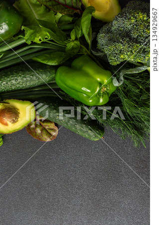 A variety of fresh green vegetables is neatly arranged on a dark surface, showcasing cucumbers, bell pepper, avocado, broccoli, and various leafy greens, healthy eating for a nutritious salad 134929667
