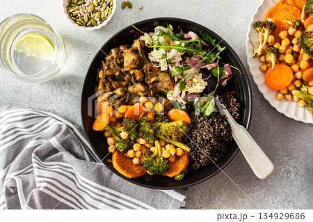 A nutritious breakfast bowl with black quinoa, avocado, roasted chicken, sweet potatoes, zucchini, and broccoli, paired with a fresh salad of cabbage, radish, chia, and sesame seeds 134929686