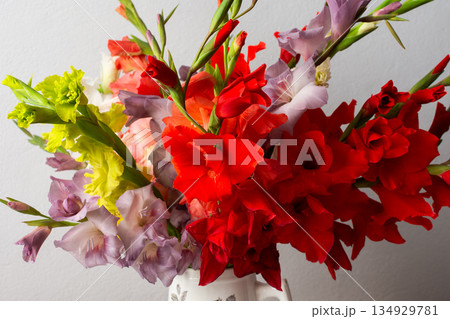A vase holds a variety of colorful gladiolus including red and white blooms. The arrangement sits on a clean surface, adding a touch of nature to the indoor space 134929781