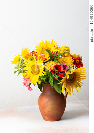 Flowers in a vase fill a space with color and texture. Sunflowers, zinnias, and greenery are mixed together. Light brightens the scene, showcasing their vibrant colors 134930060