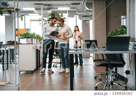 Holding eco boxes and tablet. Men and woman are working in the office together Holding eco boxes and tablet. Men and woman are working in the office together 134930167