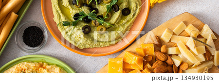 Broccoli hummus is artistically displayed in a bowl, garnished with olives. Accompanied by a charcuterie board featuring cheese, nuts, and breadsticks for a delightful snack experience, banner 134930195
