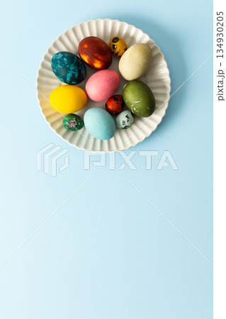 A variety of decorated Easter eggs in vibrant colors are creatively arranged on a white plate set against a soft blue background, symbolizing spring festivities and joy A variety of decorated Easter eggs in vibrant colors are creatively arranged on a white plate set against a soft blue background, symbolizing spring festivities and joy 134930205
