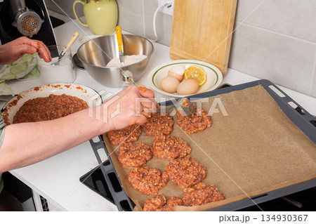 A person shapes liver cutlets on a baking tray. Mixing bowls and eggs are visible nearby, indicating food preparation in a kitchen setting during autumn A person shapes liver cutlets on a baking tray. Mixing bowls and eggs are visible nearby, indicating food preparation in a kitchen setting during autumn 134930367