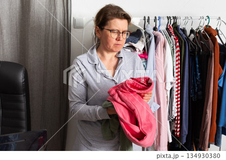 A woman stands on a balcony in the city during autumn. She holds two pieces of clothing and looks thoughtfully at her selection of home clothes in the morning A woman stands on a balcony in the city during autumn. She holds two pieces of clothing and looks thoughtfully at her selection of home clothes in the morning 134930380