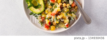 A vibrant vegetarian salad featuring boiled millet, chickpeas, fresh vegetables, and avocado, drizzled with olive oil for a delicious and healthy meal, banner 134930436