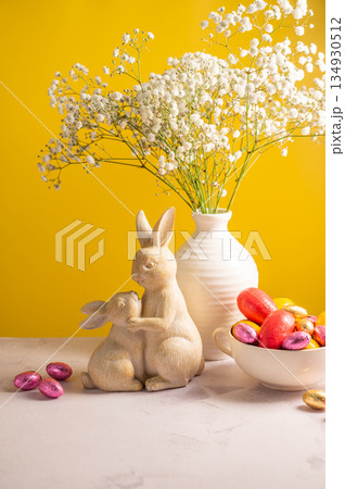 Easter chocolate colourful eggs in a bowl, cute bunnies and gypsophila flowers in a vase. Spring holiday background. Easter chocolate colourful eggs in a bowl, cute bunnies and gypsophila flowers in a vase. Spring holiday background. 134930512