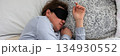 A 50-year-old woman is peacefully sleeping in a cozy bed. She wears a sleep mask and is snuggled under soft blankets, creating a serene atmosphere for rest, banner 134930552