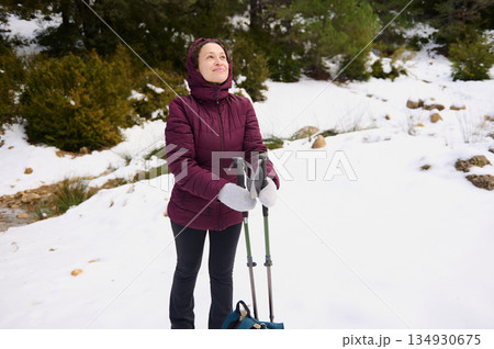 Snowy Mountain Hike With Woman In Burgundy Jacket And Trekking Poles 134930675