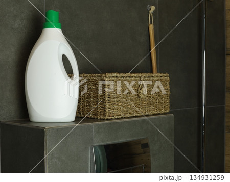 Liquid laundry detergent bottle standing next to a wicker basket in a modern bathroom interior Liquid laundry detergent bottle standing next to a wicker basket in a modern bathroom interior 134931259