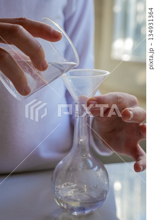 Hands Pouring Liquid into Glass Flask Vertical 134931364