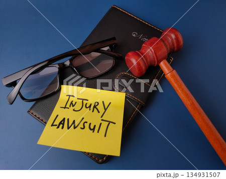 The image displays a legal concept represented by a gavel, glasses, notebook, and a sticky note with the text INJURY LAWSUIT. 134931507