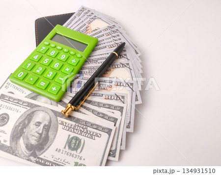 The image features a small, green electronic calculator and a pen on top of US hundred dollar bills. 134931510