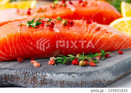 Fresh salmon fillets with herbs and citrus on a wooden cutting board at a kitchen counter ready for cooking Fresh salmon fillets with herbs and citrus on a wooden cutting board at a kitchen counter ready for cooking 134931835