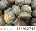 Kabocha squash pile at a market stall, displaying healthy autumnal produce with dark green skin and distinctive yellow stripes, representing organic harvest and wholesome eating 134932742