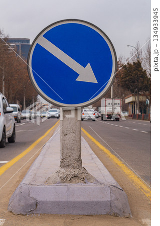 A round blue road sign indicating to drivers the directions for the end of the maneuver at the exit from the intersection with its white arrow. It is placed at intersections of two-way roads. A round blue road sign indicating to drivers the directions for the end of the maneuver at the exit from the intersection with its white arrow. It is placed at intersections of two-way roads. 134933945