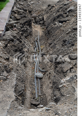 A section of dug trenches at edge of the carriageway of an asphalt road, under which black plastic pipes were laid for water supply or drainage. Repair and restoration works of underground utilities A section of dug trenches at edge of the carriageway of an asphalt road, under which black plastic pipes were laid for water supply or drainage. Repair and restoration works of underground utilities 134933947