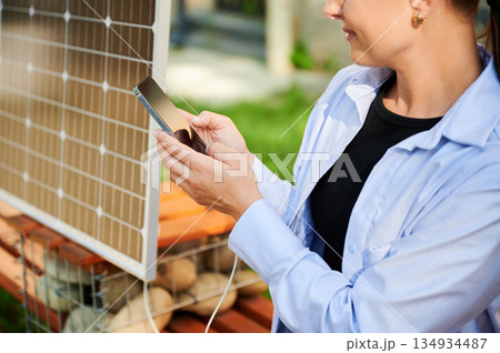 Happy woman using smartphone connected to solar panel. Cropped view. Integration of sustainable renewable energy into everyday life, demonstrating practical use of solar power for charging devices. Happy woman using smartphone connected to solar panel. Cropped view. Integration of sustainable renewable energy into everyday life, demonstrating practical use of solar power for charging devices. 134934487