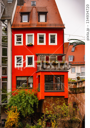 Bright Red Historic House In Nuremberg: Traditional German Architecture With Wooden Balcony And Vibrant Facade Surrounded By Autumn Foliage 134934720