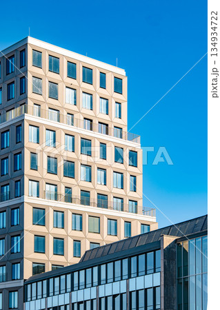 Modern Office Tower In Munich: Contemporary Urban Architecture With Geometric Facade And Glass Windows Under Clear Blue Sky 134934722