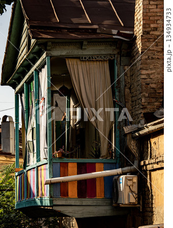 Old Wooden Balcony In Tbilisi Georgia: Weathered Architecture With Peeling Paint, Rustic Windows, And Hanging Laundry In Evening Light Old Wooden Balcony In Tbilisi Georgia: Weathered Architecture With Peeling Paint, Rustic Windows, And Hanging Laundry In Evening Light 134934733