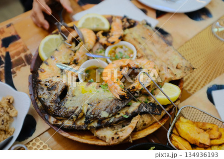 Portuguese grilled seafood platter with prawns sardines lemon wedges fries salad bread overhead flat lay rustic restaurant table family style dinner. High quality photo 134936193