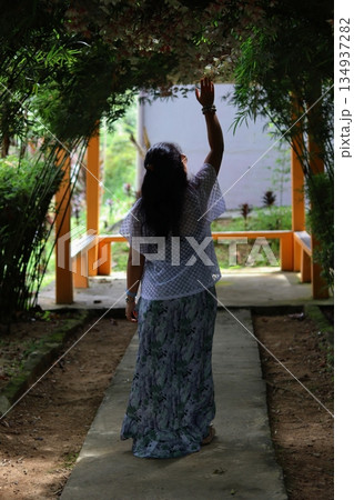 Woman walking along a garden pathway in Cameron Highlands, Malaysia, surrounded by lush plants and natural shade, expressing peaceful nature travel. Woman walking along a garden pathway in Cameron Highlands, Malaysia, surrounded by lush plants and natural shade, expressing peaceful nature travel. 134937282