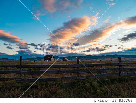 Scenic landscape features wooden fence, farm house, and dramatic sunset clouds over a rural area in the evening Scenic landscape features wooden fence, farm house, and dramatic sunset clouds over a rural area in the evening 134937763