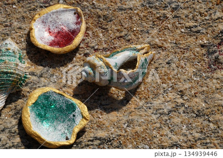 Seashells on a stone background. Several colorful, shiny seashells lie on a multi-colored stone.Seashells on a stone background. 134939446